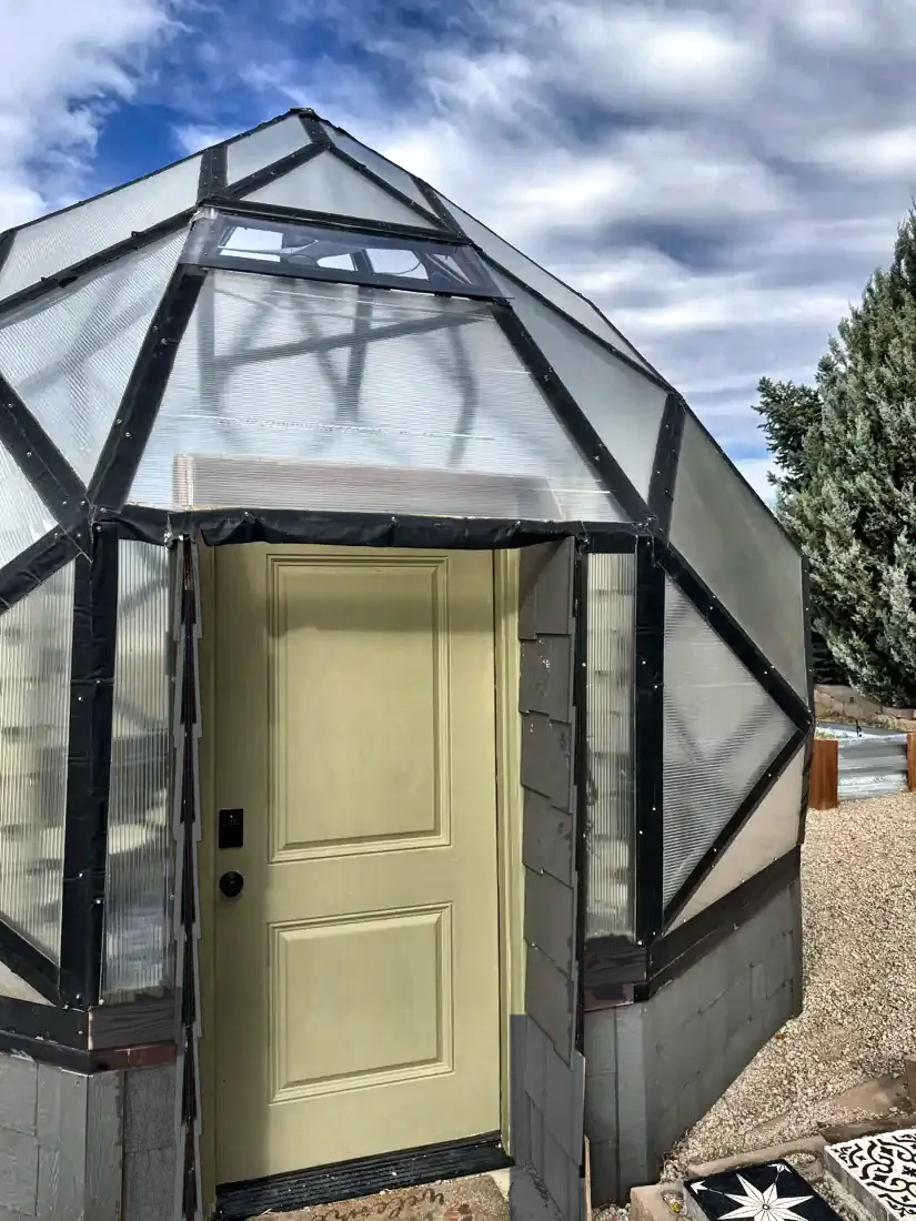 The zome's sage-green entry door framed into the pony wall, with polycarbonate panels above.