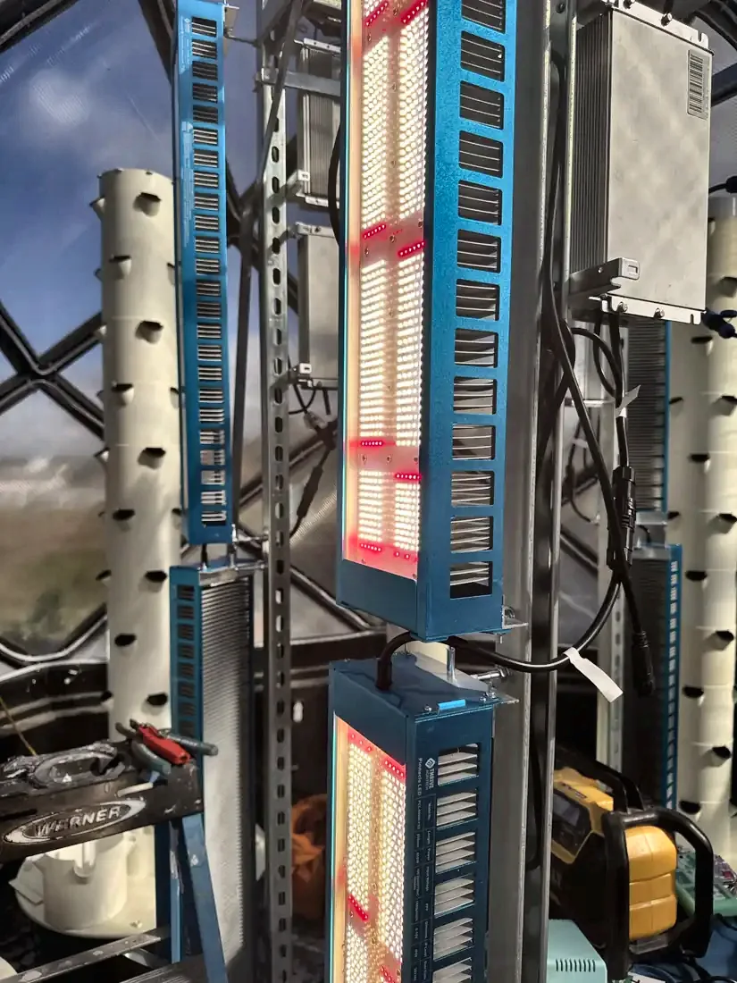 Blue-framed vertical LED grow light bars glowing red and white beside a tower.