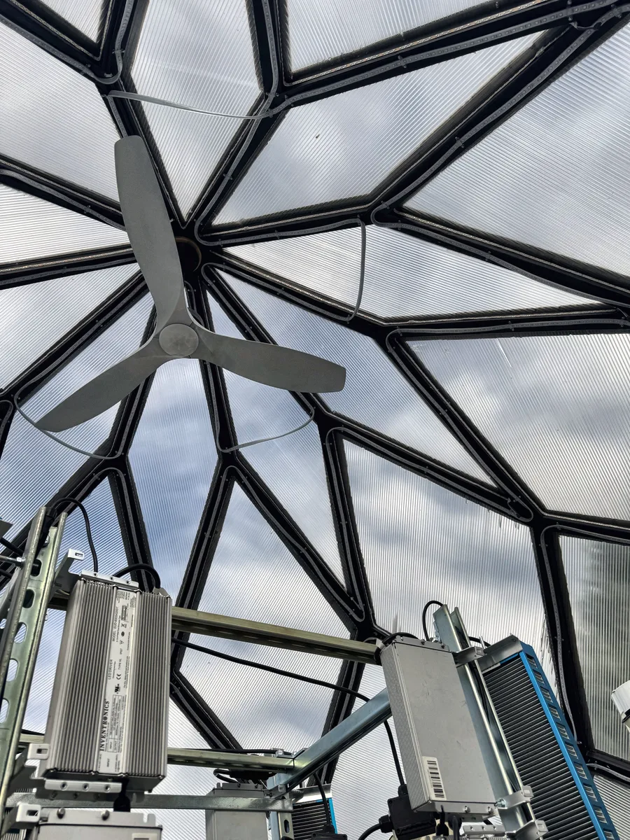 Looking up at the apex from inside: a ceiling fan under the ten-point star of struts, with LED drivers on the light rack below.
