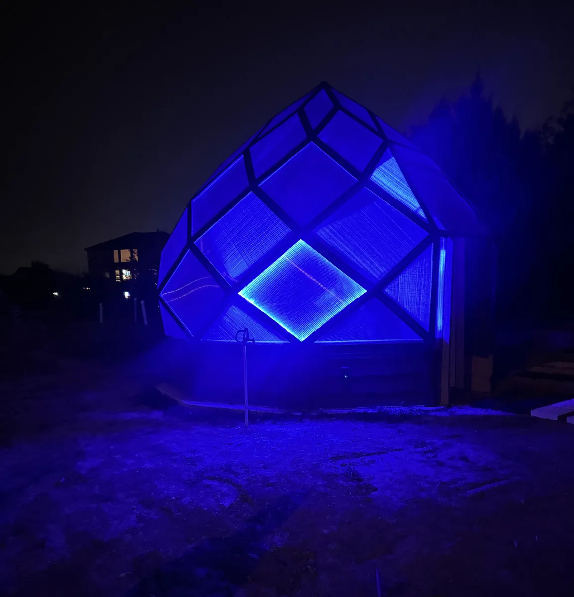 The zome at night glowing deep blue from LED strips along its struts.
